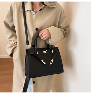 Detail of a matte black textured leather handbag worn with a beige trench coat