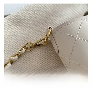 Close-up of golden metal hooks and chain strap on a white quilted leather bucket bag