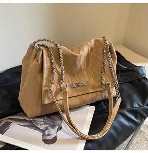 Close-up of khaki wrinkled leather tote with silver chain and metal logo plaque