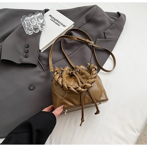 Close-up of brown quilted bucket bag with braided handle and drawstring on grey blazer
