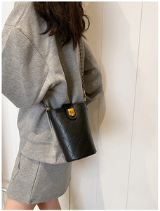Detail view of a black quilted bucket bag with gold chain strap on a model's shoulder