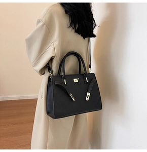 Side view of a black leather handbag with gold hardware worn with a beige coat