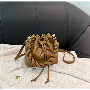 Close-up of brown quilted bucket bag with woven handle and adjustable strap on white tweed