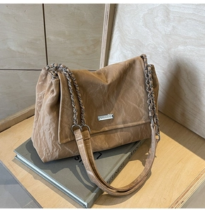 Detail of khaki pleated tote bag featuring silver chain strap and metal logo plaque