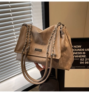 Detail of beige tote bag featuring textured leather and brand metal plaque accent