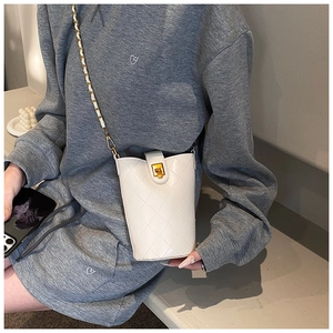 Detailed view of a white quilted bucket bag with gold lock and chain strap on a model