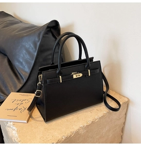 Close-up of black lychee leather handbag with gold twist lock and adjustable shoulder strap