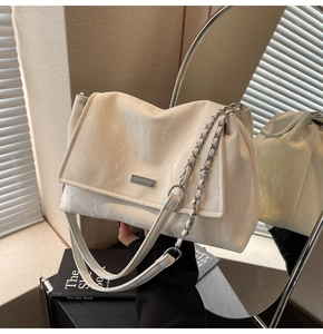 Detail of cream white pleated tote bag with chain strap and metallic logo on mirrored base