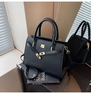 Detail of black lychee grain leather handbag with gold metal lock on beige background
