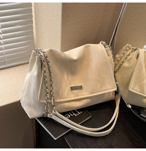 Detail of ruched textured beige tote bag with silver chain strap and logo plaque