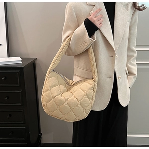 Minimalist beige quilted crescent shoulder bag with silver zipper on elegant model outfit