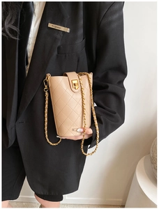 Detail of beige quilted bucket bag with gold chain strap worn with black blazer