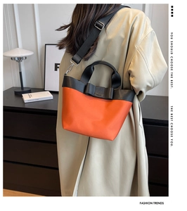 Detail of orange and black bucket bag with bow ornament and wide woven shoulder strap