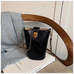 Close-up of quilted black bucket bag with gold metal lock and chain strap on art books
