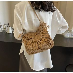 Close-up of handwoven straw bag with fringe details and woven shoulder strap for summer