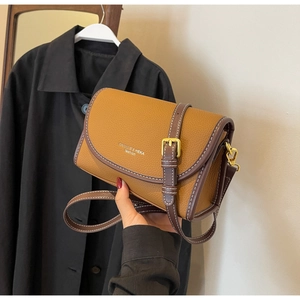 Détail d'un sac bandoulière en cuir marron avec bandoulière contrastée et boucle dorée