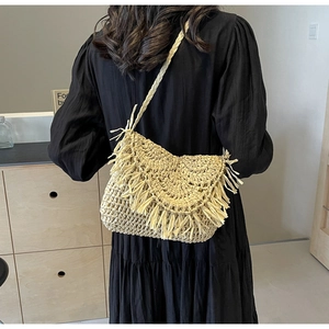 Close-up of beige straw shoulder bag with fringe detail and woven strap on model