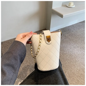 Detail of white quilted bucket bag with gold chain strap and elegant metallic buckle