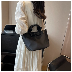 Detail showing elegant black nylon bucket bag with large decorative bow on white pleated skirt
