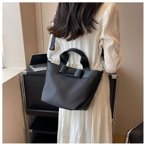 Detail of black nylon bucket bag featuring a large bow and adjustable shoulder strap