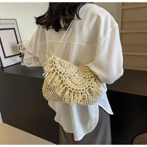 Detail of cream woven straw crossbody bag with decorative fringe and long strap