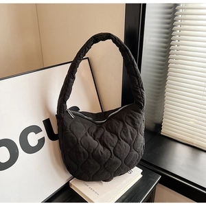 Close-up of a black quilted nylon shoulder bag with silver zipper on white books