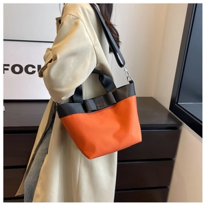 Detail of orange nylon bucket bag featuring a black bow and adjustable shoulder strap