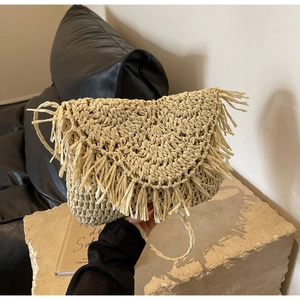 Detailed close-up of straw woven crossbody bag featuring fringe trim on stone surface