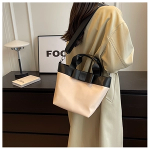 Close-up of beige nylon bucket bag with black bow detail and adjustable woven shoulder strap