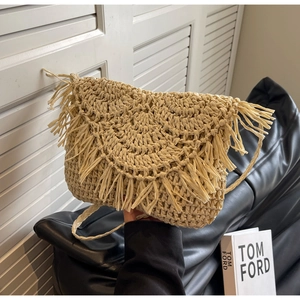 Macro shot of beige woven straw crossbody bag featuring boho fringe and triangle flap