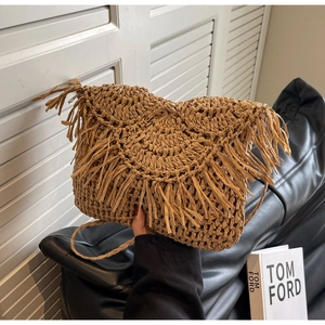 Detail of a khaki woven straw crossbody bag with bohemian fringe and a braided strap