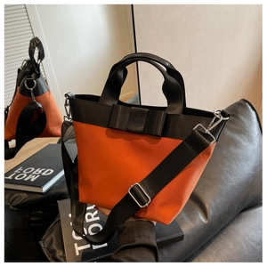 Detail of bright orange nylon bucket bag featuring black bow and wide crossbody strap