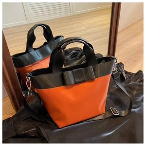 Detail of orange nylon bucket bag with black bow handles and detachable shoulder strap