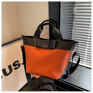 Detail of a vibrant orange nylon bucket bag with a black bow and wide shoulder strap