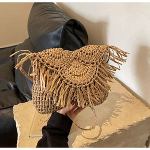 Detailed view of woven straw bag with decorative fringe and long braided shoulder strap
