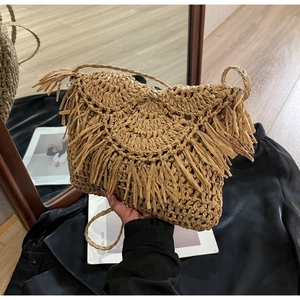 Detail of straw woven crossbody bag with layered fringe and long shoulder strap