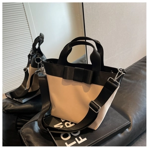 Detail of beige nylon bucket bag with large black bow and adjustable wide shoulder strap