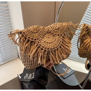Close-up of woven straw bag with long fringe tassels and delicate metal zipper detail