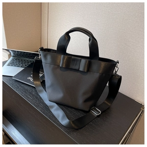 Detail of black nylon tote bag with bow accent and detachable strap on office desk