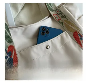 Detail of off-white nylon tote with functional front pocket and floral embroidery