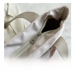 Detail of a smooth silver metal zipper on an off-white nylon tote bag with woven handles