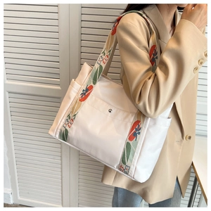 Close-up of white nylon tote bag featuring a colorful embroidered wide shoulder strap