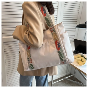 Close-up of beige tote bag featuring floral embroidered wide strap and side pocket detail