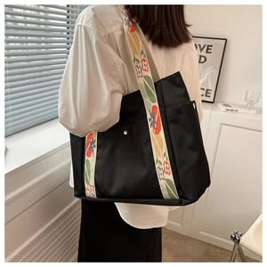Detail of black nylon tote bag featuring colorful floral embroidered wide shoulder strap
