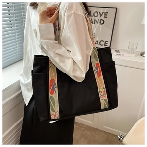Detail of a black nylon tote bag featuring colorful floral embroidered straps and side pocket