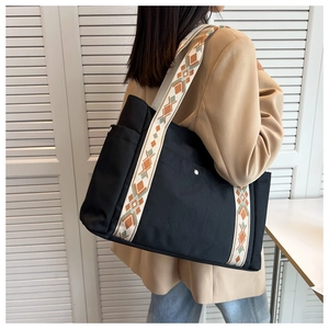 Detail of black nylon tote bag featuring ethnic embroidered wide shoulder strap and side pocket