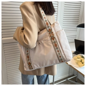 Detail of a cream nylon tote bag with wide vintage jacquard strap and functional pockets