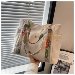 Detail of white nylon tote bag featuring colorful floral woven strap and metal magnetic closure