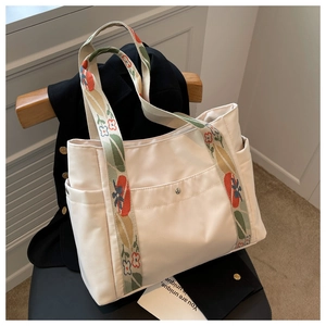 Detail view of cream nylon tote bag with colorful floral embroidered shoulder strap