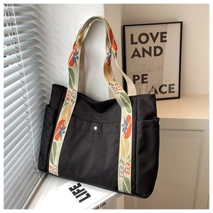 Detail of black nylon tote bag featuring floral print handles and front snap pocket